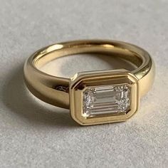 a gold ring with a baguette cut diamond in the center, on a gray surface