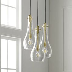 three clear glass light bulbs hanging from a ceiling fixture in a white room with windows