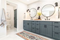 a bathroom with double sinks and mirrors on the wall, rug in front of it