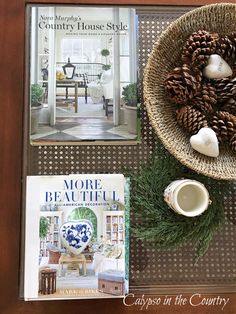 pine cones and other decorations sit on a tray next to a book, coffee cup, and magazine