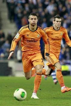 two soccer players in orange uniforms are playing with a ball on the field while people watch from the stands