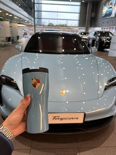 a hand is holding a cup in front of a blue sports car at a showroom