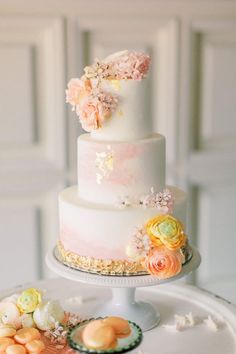 a three tiered wedding cake with flowers on the top and sides, sitting on a table