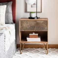 a nightstand with some books on it next to a bed and a white rug in a bedroom