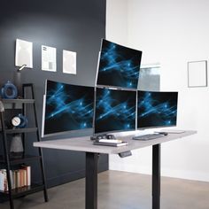 three computer monitors sitting on top of a desk in front of a book shelf and bookshelf