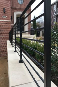 a black metal fence on the side of a brick building next to bushes and trees