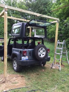 a jeep parked under a wooden structure in the grass next to a ladder and trees