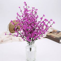 purple flowers are in a glass vase on a table next to a book and scarf