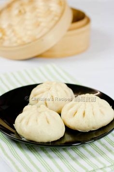 three small dumplings on a black plate next to two wooden bowls and napkins