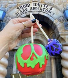 a hand holding two skewers in front of a building with a skull on it