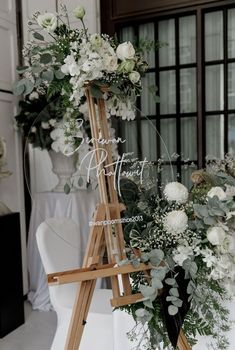 a wooden easel with flowers and greenery on it for a wedding ceremony sign