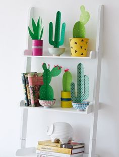 a white shelf filled with potted plants next to a wall mounted cactus plant on top of it