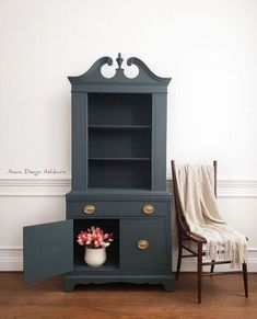 a blue cabinet sitting next to a chair and a white vase with flowers in it