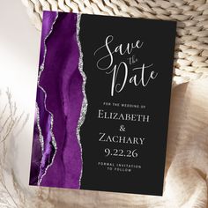 a purple and black wedding save the date card with silver foil on it next to a wicker basket