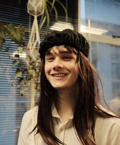 a woman with long hair wearing a black hat and white shirt smiling at the camera