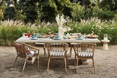 a table with chairs and plates on it in the middle of a garden surrounded by tall grass