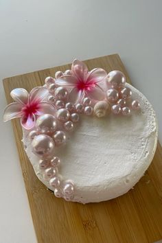 a cake decorated with flowers and pearls on a wooden cutting board next to a knife