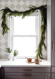 a kitchen window with evergreen garland hanging over it