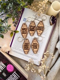 four wooden keychains sitting on top of an open book next to some flowers