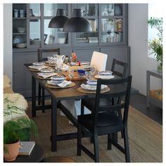 a dining room table with plates and cups on it, next to an open bookcase