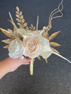 a hand holding a flower bouquet with gold leaves and flowers on the top of it