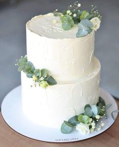 a three tiered white cake with greenery on top