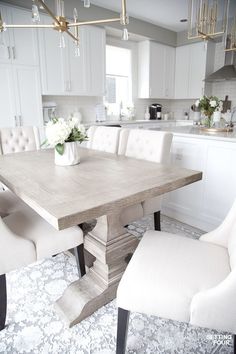 a dining room table with white chairs and flowers in a vase on the centerpiece