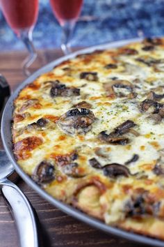 a pizza sitting on top of a pan next to two glasses of wine and utensils