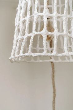 a close up of a light fixture made out of white wire and rope with a small bird on it's back end