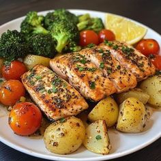 salmon, potatoes and broccoli on a plate with lemon wedged cherry tomatoes