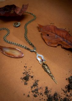 "Made from a slice of a geode and faceted garnet, this matinee-style necklace embodies the cavern chalice.  It is a fertility shrine around your neck. Both styles feature a neutral colored geode slice (exact shade and shape vary) and faceted garnet on a vintage boxchain or thinner curb chain. A dark bronze filigree \"stalactite\" dangles from the bottom of the pendant. Neckline, 18\" with 3\" adjuster Pendant drop 5\" -Vintage brass chain with brass overlay -Geode slice charm  -Garnet" Spiritual Bronze Agate Jewelry, Unique Brass Teardrop Necklaces, Spiritual Hand Forged Medallion Necklaces, Spiritual Hand Forged Medallion Necklace, Hand Forged Agate Pendant Necklace, Hand-forged Agate Pendant Necklace, Spiritual Teardrop Brass Necklaces, Spiritual Hand Forged Oval Pendant Necklace, Spiritual Teardrop Brass Necklace