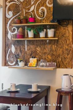 a wall mounted tv sitting above a wooden shelf filled with cups and saucers on top of a table