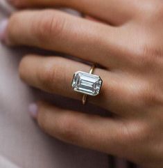 a close up of a person wearing a ring with an emerald cut diamond on it