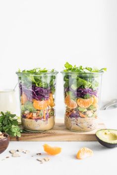 two mason jars filled with salad ingredients on a white surface next to an avocado slice