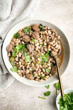 a white bowl filled with beans and greens next to a spoon on top of a table