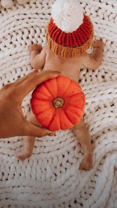 a baby laying on top of a white blanket next to a stuffed pumpkin and a knitted hat