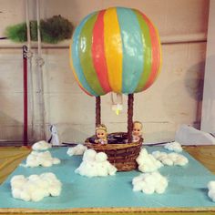 two small children in a hot air balloon on top of a blue surface with white clouds