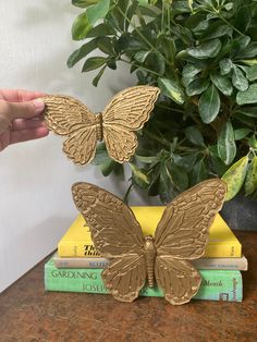 a gold butterfly sculpture sitting on top of some books next to a potted plant