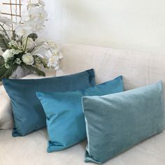 three blue pillows sitting on top of a white couch next to a vase with flowers