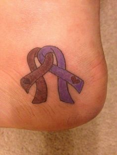 a foot with a purple and brown ribbon tattoo on it's side, next to a pink heart