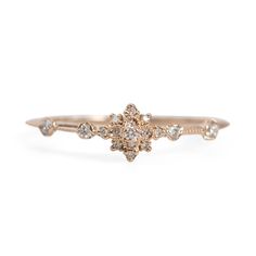 a gold ring with diamonds on the side and a small flower in the middle, sitting on top of a white background