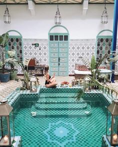 a woman sitting on the edge of a swimming pool in front of a building with tiled walls