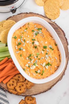 a white bowl filled with carrot dip surrounded by crackers, celery and pretzels