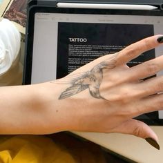 a woman's hand with a bird tattoo on her left wrist next to a laptop