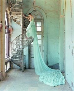 a woman in a blue dress standing on a spiral staircase