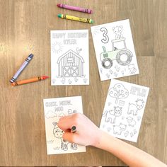 a child's hand with crayons and coloring paper on a wooden table