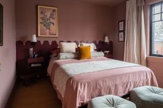 a bedroom with pink walls and white bedding, two stools on either side of the bed