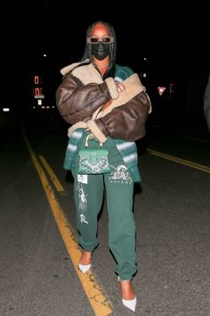 a man wearing a mask and green sweatpants is walking down the street at night