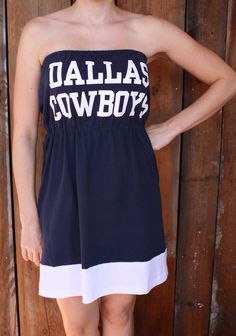 a woman standing in front of a wooden fence wearing a dress with the word dallas cowboys on it