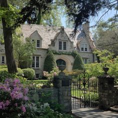 a large house surrounded by lush green trees and flowers in front of it's gate